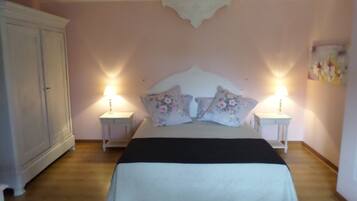 Un dormitorio con una cama, dos mesitas de noche con lámparas, un armario y un cuadro con motivos florales en la pared.