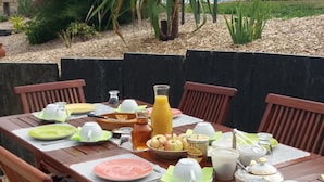 An outdoor dining table set with plates, cutlery, and various food items, surrounded by wooden chairs. - Chambres d'Hôtes La Rompardais (Pleven)