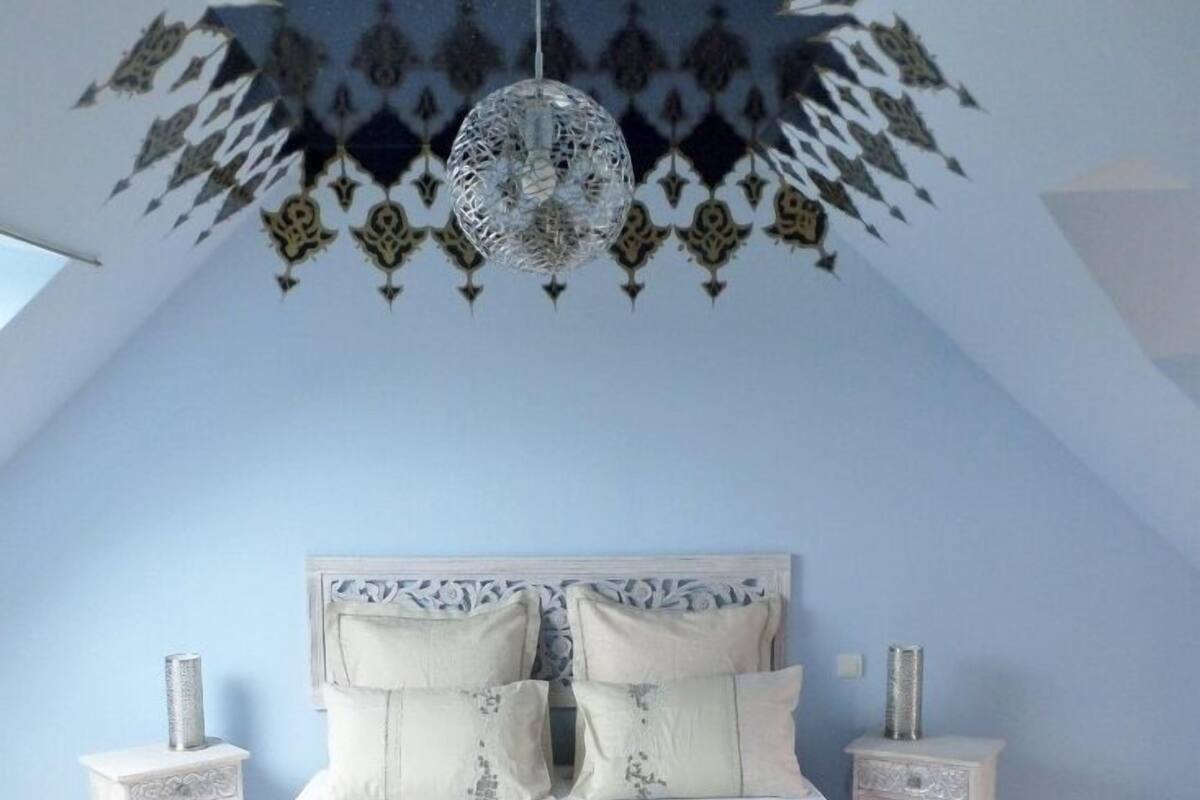 Un dormitorio con una cama, dos mesitas de noche, una lámpara colgante y un techo estampado.