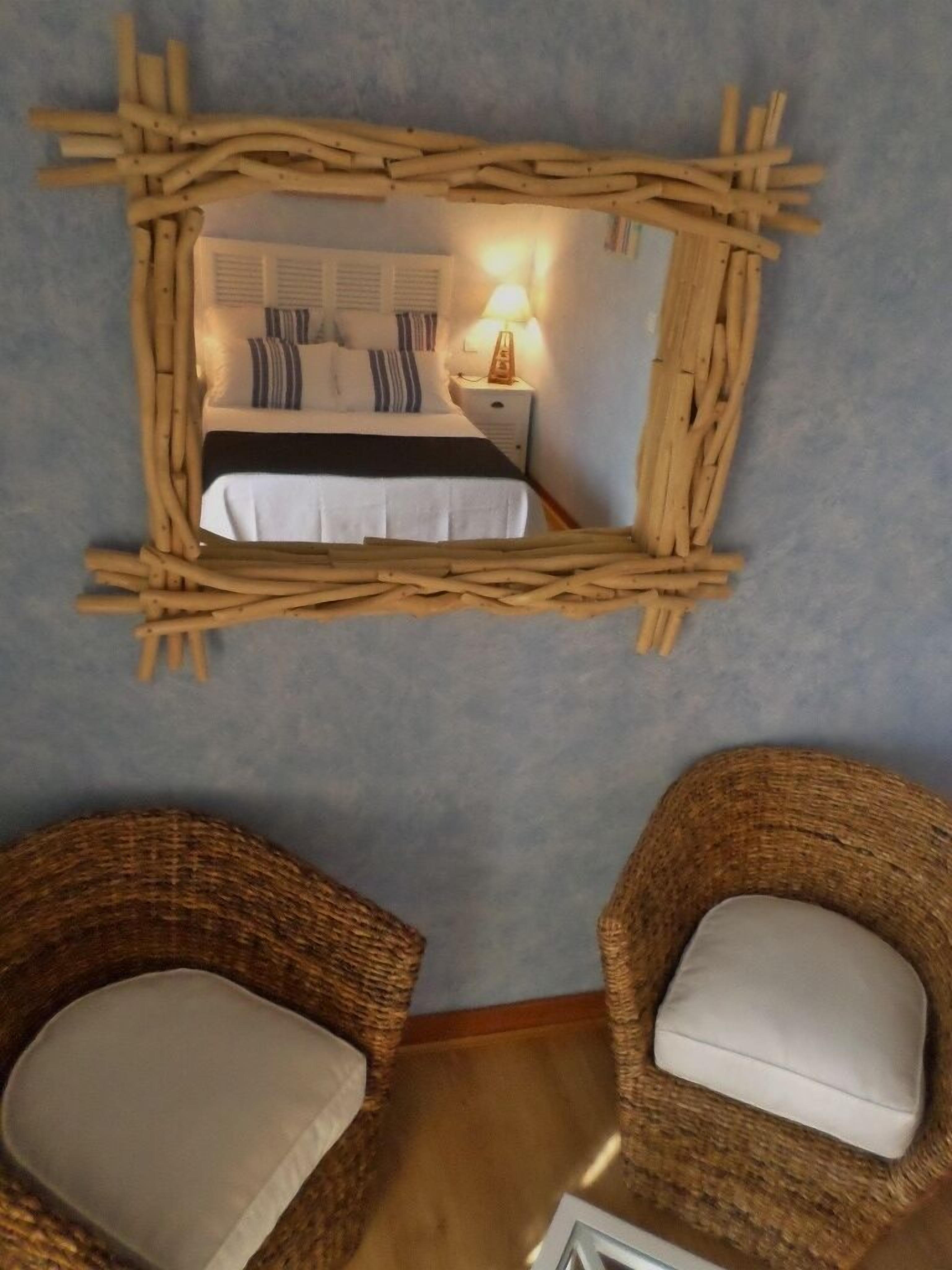 Een slaapkamer met een bed, nachtkastje, lamp en twee rieten stoelen.