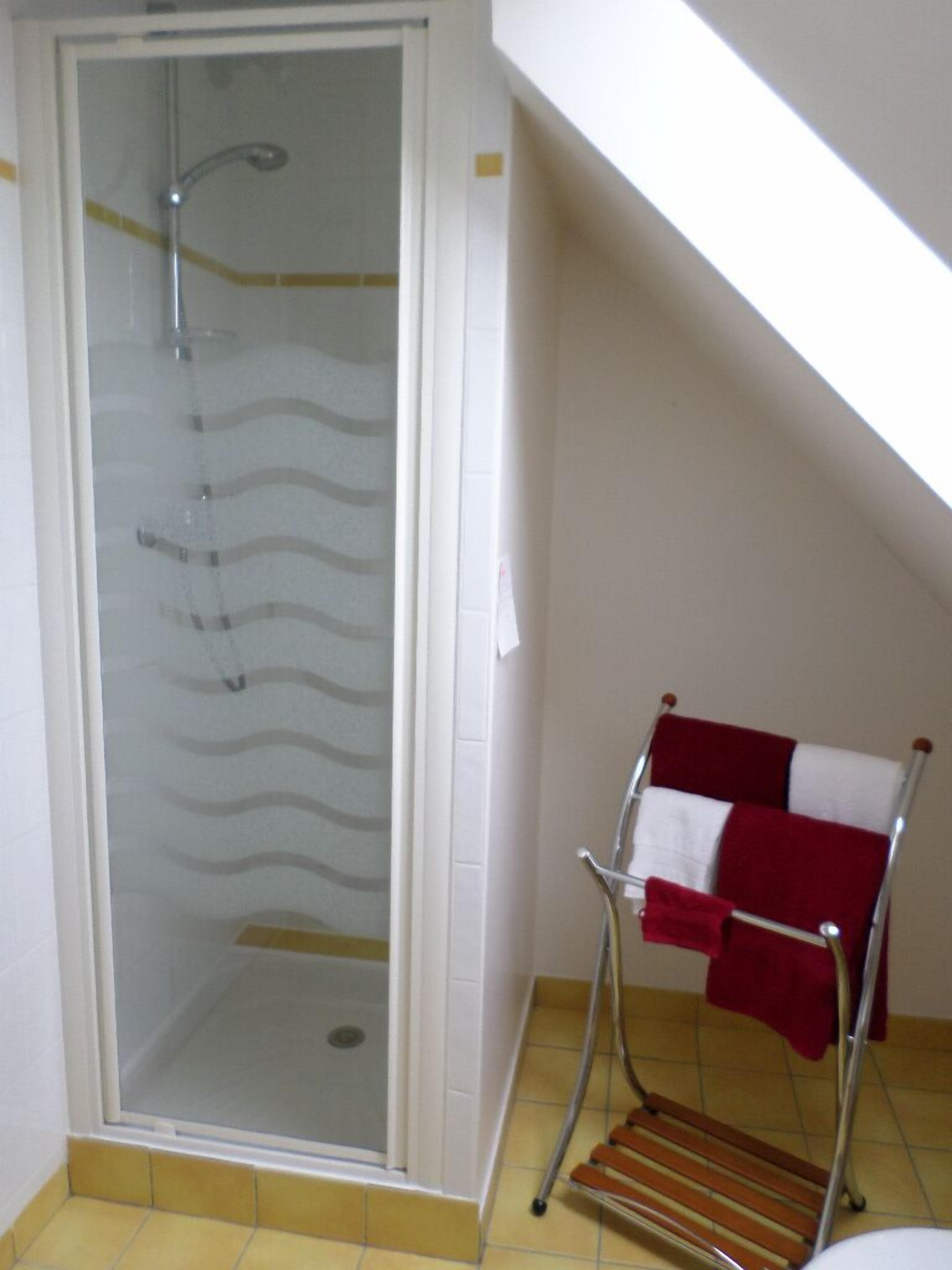 Ducha con puerta de cristal, toallero metálico con una toalla roja y un banco de madera.