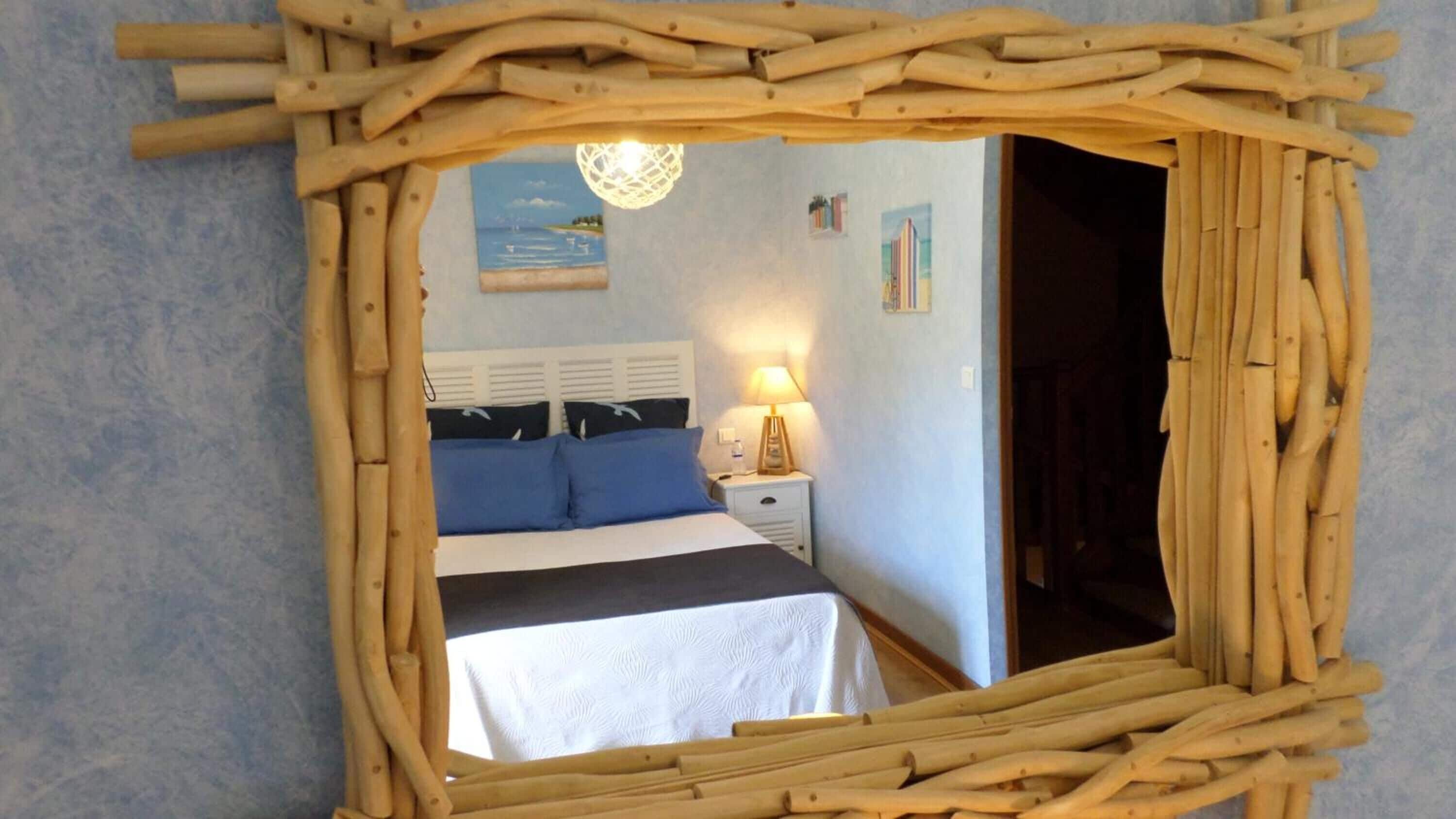 A bedroom with a bed, bedside table, lamp, and a view of the sea through a window.
