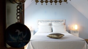 A bedroom with a white bed, a decorative headboard, and a nightstand with a lamp. - Chambres d'Hôtes La Rompardais (Pleven)