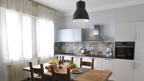 A modern kitchen with white cabinets, a wooden dining table, and a black pendant light.