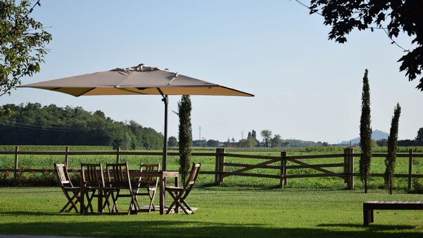 An outdoor seating area with a table and chairs under a large umbrella, surrounded by a wooden fence and greenery.