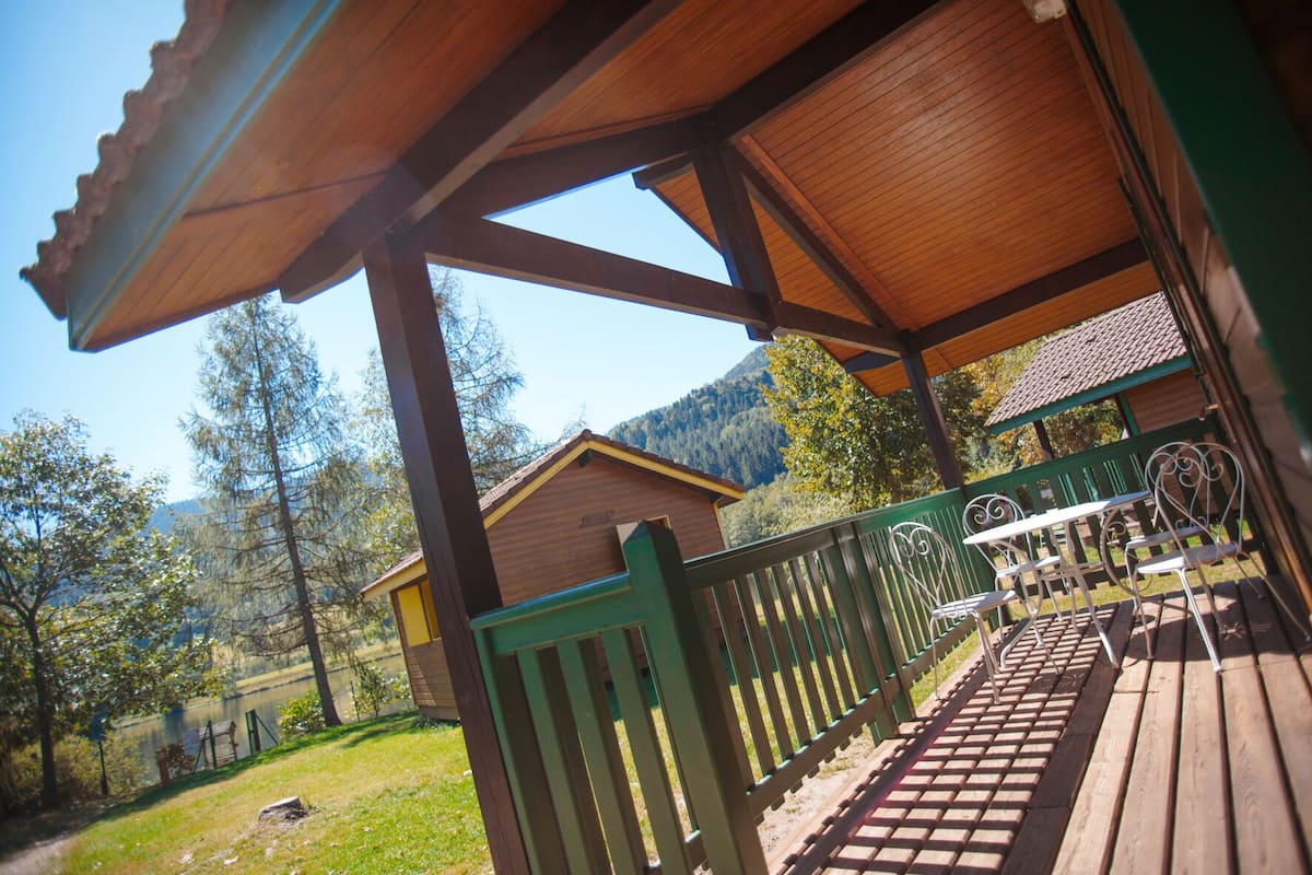 Una terraza de madera con baranda verde, un área de estar cubierta y vista a una montaña y un bosque.
