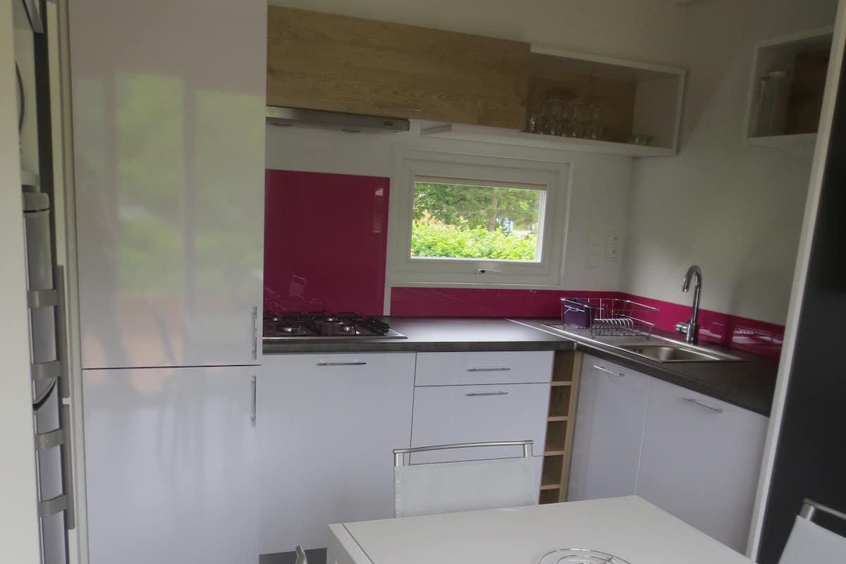 Una cocina compacta con una mesa y sillas blancas, una ventana con vistas a zonas verdes y un horno empotrado.