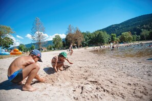 A sandy beach with people playing and swimming in the water. - Base de Loisirs du Lac de la Moselotte (Saulxures-sur-Moselotte)