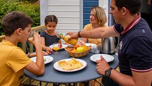 A family dining outdoors at a table with plates of food, a basket of fruit, and a kettle. - Base de Loisirs du Lac de la Moselotte (Saulxures-sur-Moselotte)