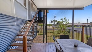 A covered outdoor area with a wooden deck, a metal staircase, and a view of a residential street. - Evans Above - 1-5 Wattle Street (EVANS HEAD)