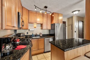 A modern kitchen with wooden cabinets, a stainless steel refrigerator, a dishwasher, and a granite countertop.