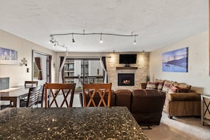 A modern living room with a fireplace, a dining area with a marble table, and a large window.