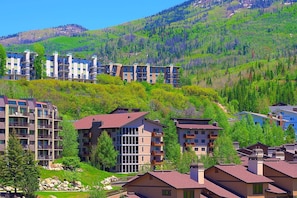 A residential area with multi-story buildings, some with balconies, set against a backdrop of green hills and trees.