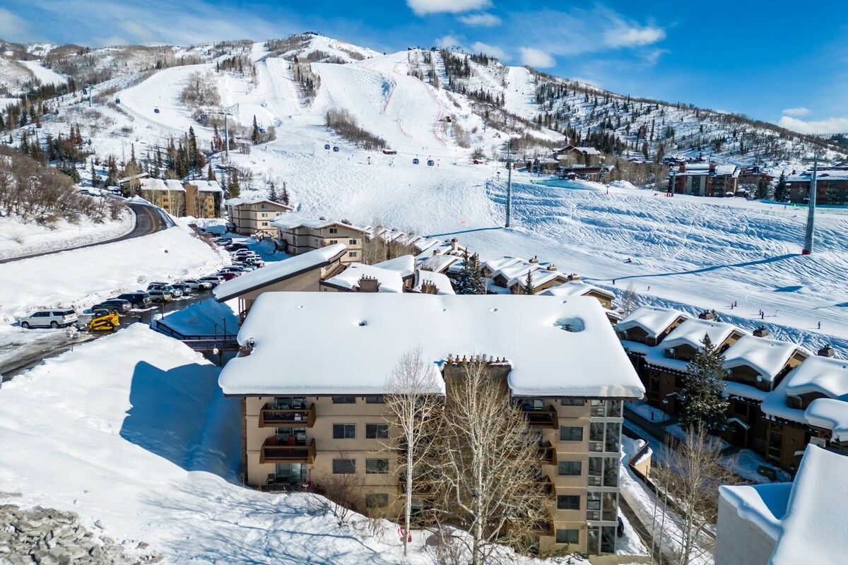 A snow-covered mountain town with a ski resort, including a building with multiple floors and a ski lift in the background.