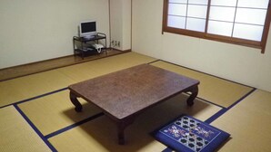 Une pièce avec un sol recouvert de tatamis, une table également en tatami, une petite étagère sur laquelle se trouve un ordinateur portable, et une fenêtre à carreaux.