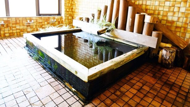 Un onsen japonais traditionnel, avec une source d’eau chaude rectangulaire, des bancs en bois et un mur recouvert de carreaux.