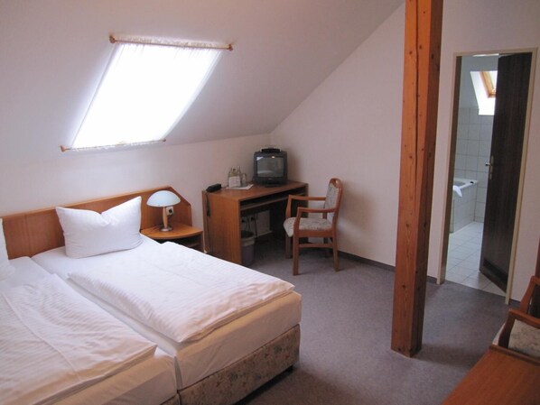 Un dormitorio con una cama, un escritorio con televisión, una silla y un ventanal pequeño.