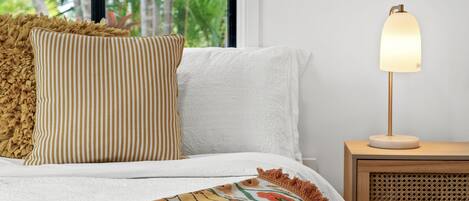 A neatly made bed with striped pillows, a patterned throw, and a bedside lamp on a wooden nightstand.