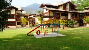 Ein Spielplatz mit Rutsche und Klettergerüst auf einer Rasenfläche, im Hintergrund sind Gebäude zu sehen.