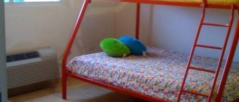 A bunk bed with a ladder, a colorful striped rug, and a red bench.