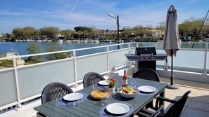 An outdoor dining area with a table set for two, a grill, and a view of a marina. - Magnificent,  spacious first floor apartment with wonderful views (Agde)