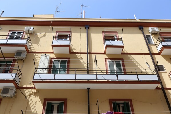 A multi-story building with balconies, air conditioning units, and a clear blue sky.