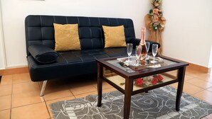 A dark blue sofa with two gold cushions, a glass coffee table with a bottle and glasses, and a floral decoration on the wall. - LA CASA DEI PARGOLI, apartment ideal for pleasant holidays in Matera (Matera)