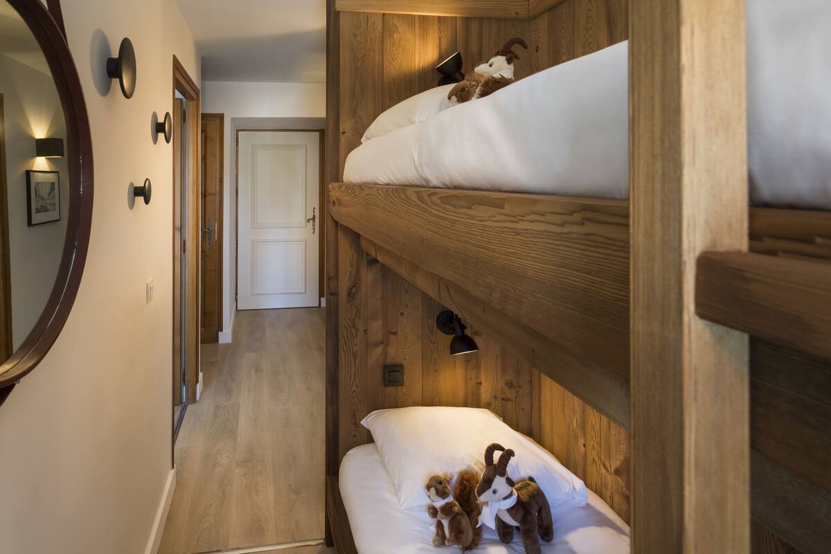 Quarto com beliches, paredes de madeira, espelho e porta ao fundo.
