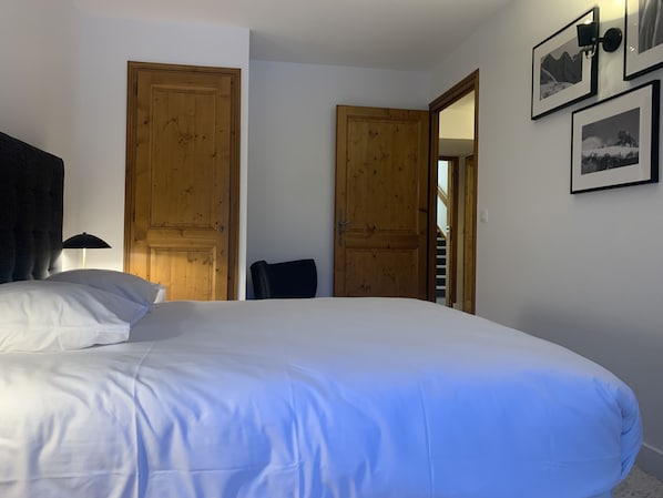Une chambre à coucher avec un grand lit, deux portes en bois, une chaise et une lampe.