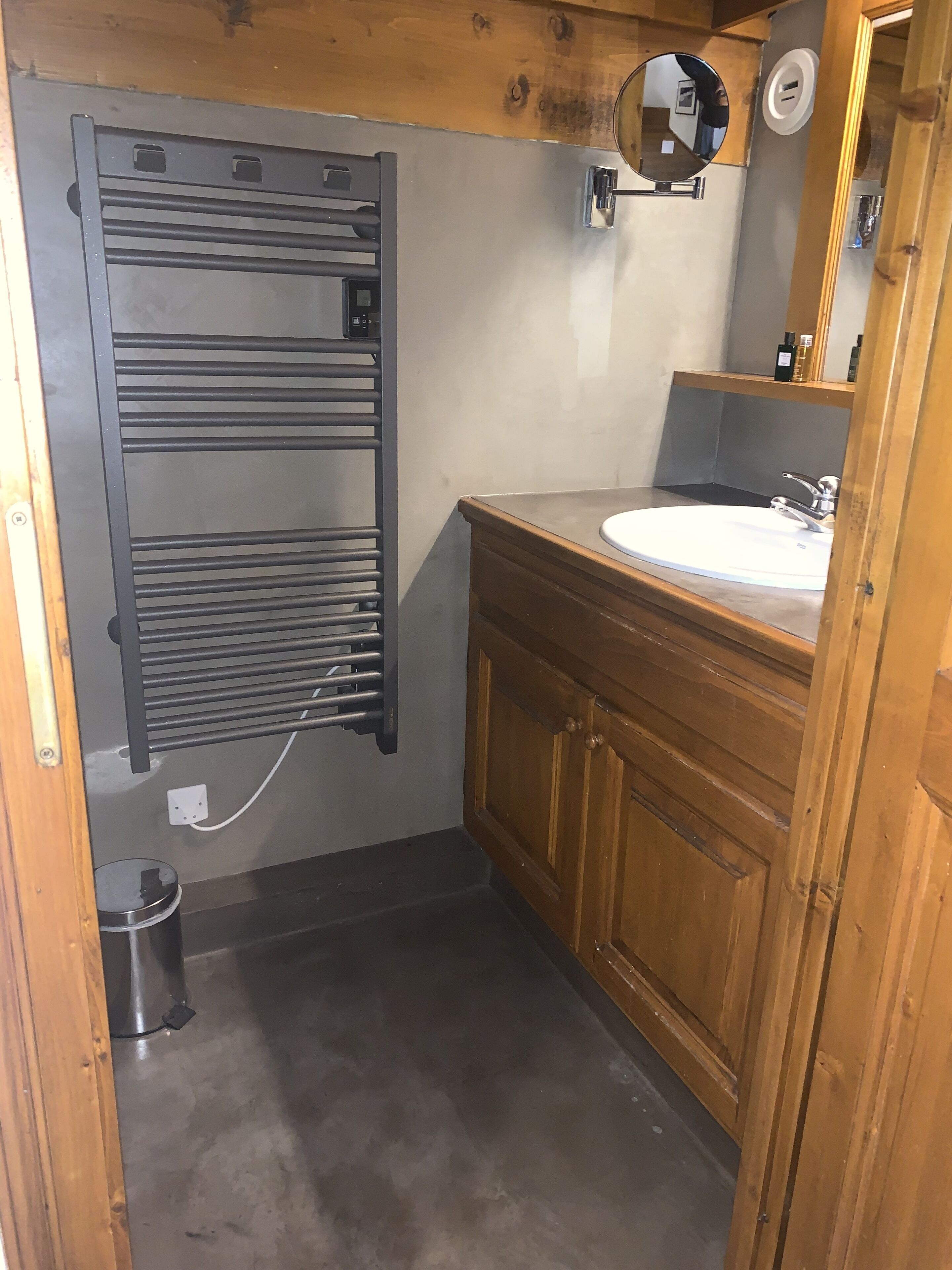 A bathroom with a wooden vanity, a white sink, a mirror, and a towel rack.