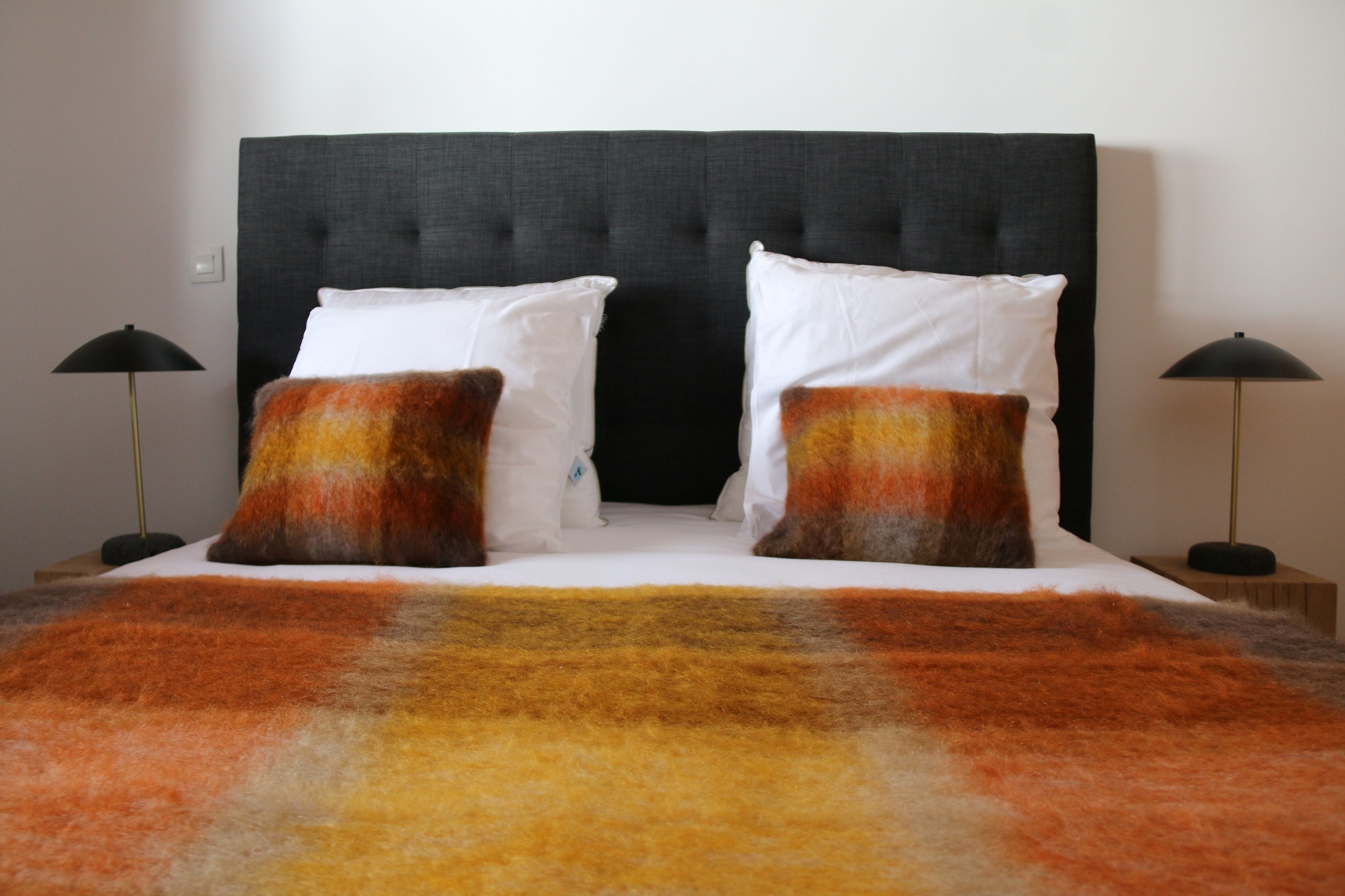 A bed with a black headboard, two white pillows, and two orange and brown throw pillows. There are two black floor lamps on either side of the bed.