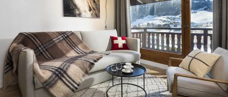 Una sala de estar acogedora con un sofá, un sillón, una mesa de centro y un ventanal con vistas a una montaña nevada.