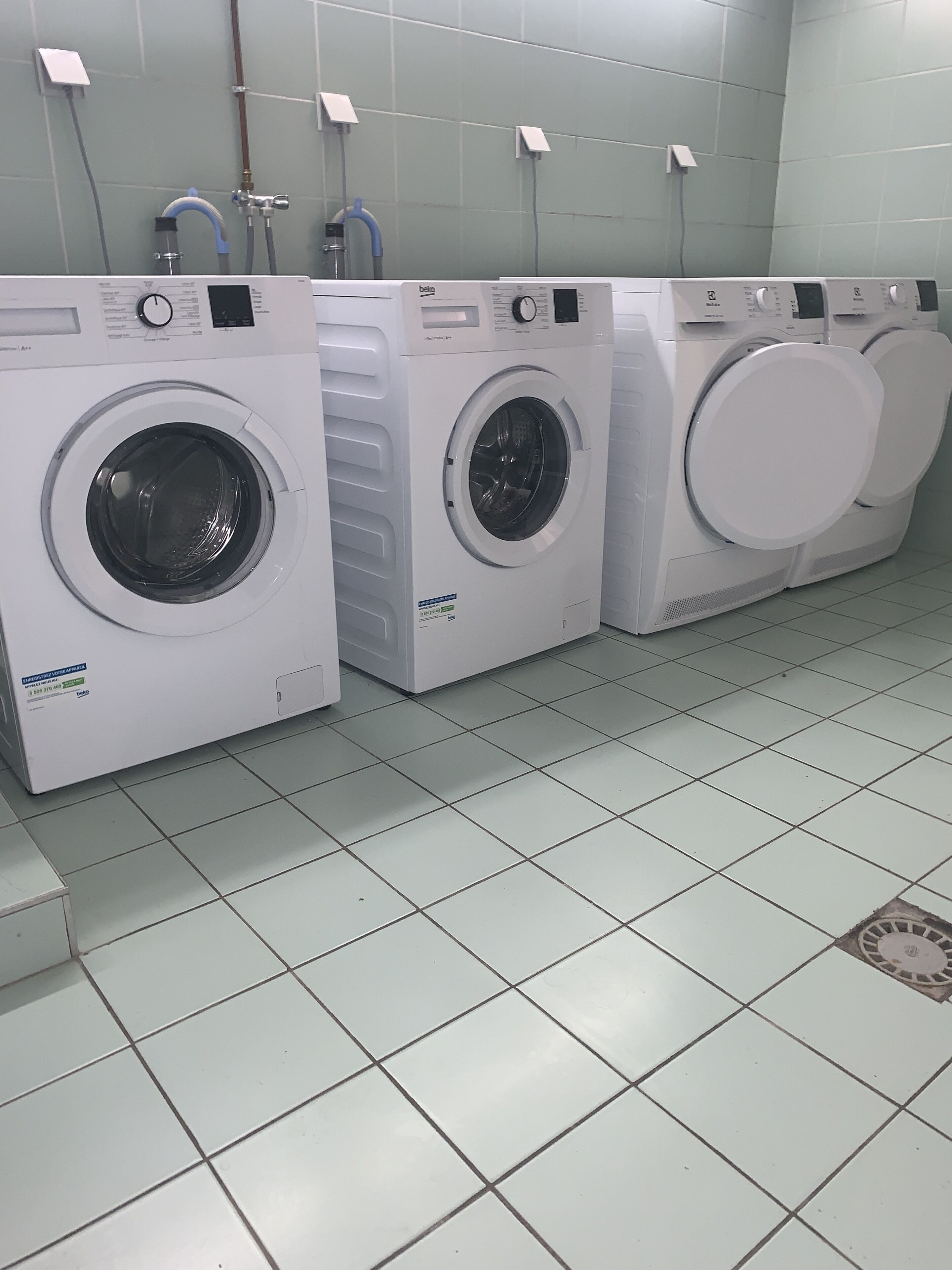 Filas de lavadoras de carga frontal blancas en una habitación con baldosas.
