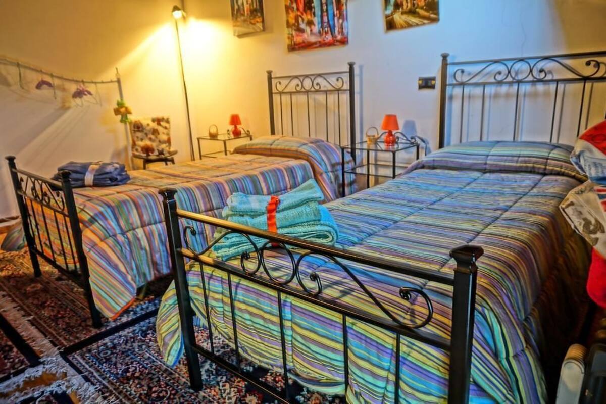 A room with two beds, each with striped bedding, a small table with a lamp, and a chair.