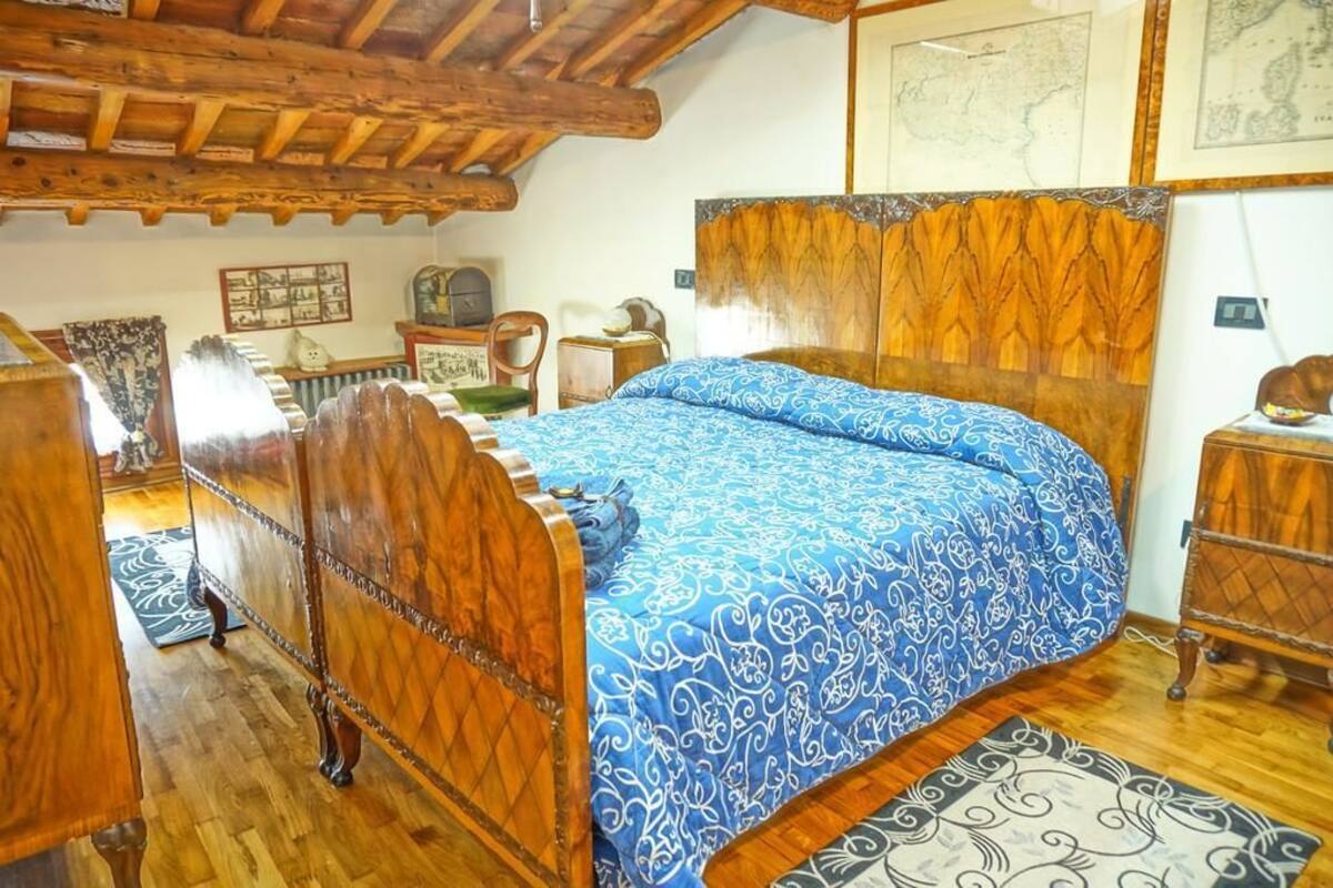 A wooden bed with a blue patterned bedspread in a room with wooden beams on the ceiling and a wooden headboard.