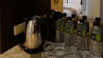 A hotel room with a minibar shelf stocked with tea and coffee, a kettle, and bottled water.