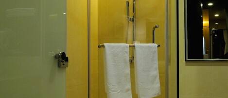 Ducha envuelta en vidrio con cabezal de ducha de mano, toallero con dos toallas y un felpudo blanco en la entrada.