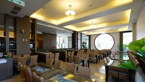 Eine geräumige Hotelhalle mit mehreren Gastronomiebereichen, großen Fenstern und modernen Leuchten.