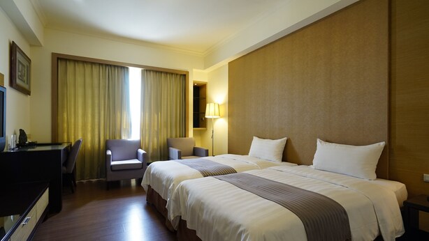 Ein Hotelzimmer mit zwei Betten, einem Schreibtisch, einem Stuhl und einer Lampe.