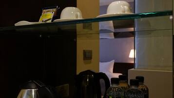 A kitchen area with a kettle, a coffee maker, and a tray with glasses and bottles.