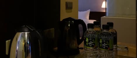 A kitchen area with a kettle, a coffee maker, and a tray with glasses and bottles.