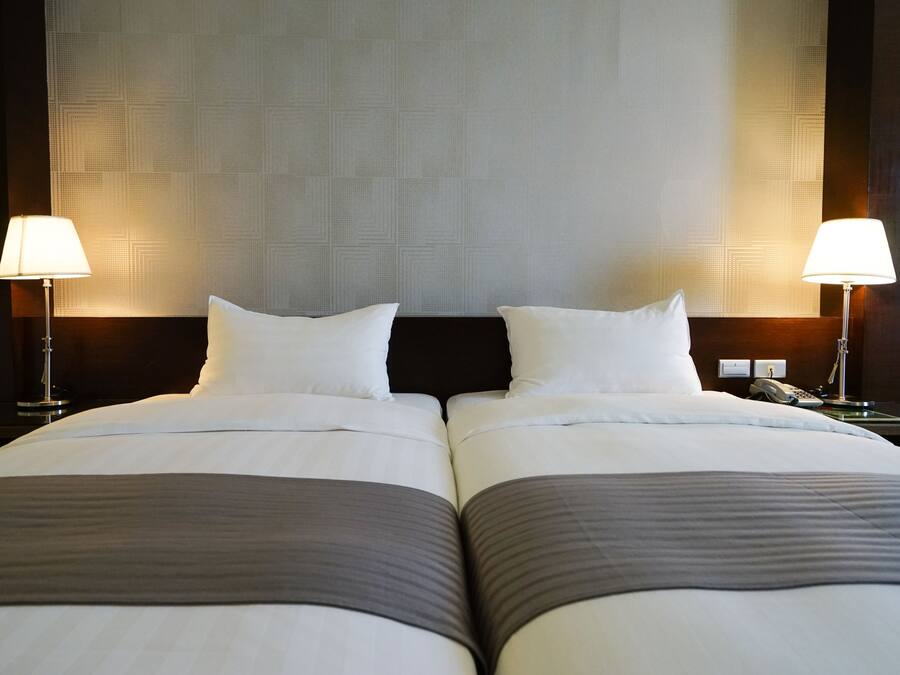 Ein Hotelzimmer mit zwei Betten, jedes mit einem Kissen und einer Lampe.