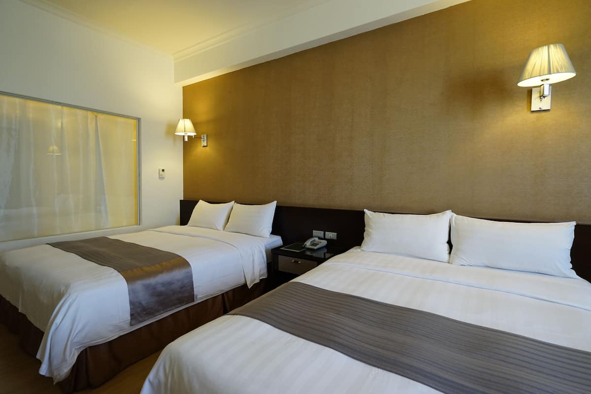 Una habitación de hotel con dos camas, una mesita de noche, una lámpara y un ventanal con cortinas.