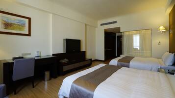 A hotel room with two beds, a desk, a chair, a television, and a painting on the wall.