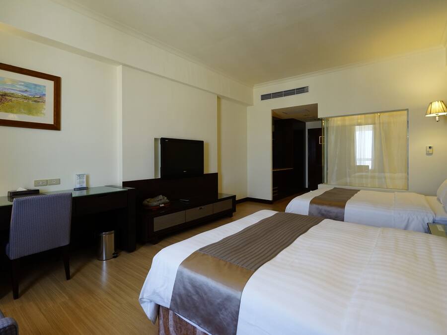A hotel room with two beds, a desk, a chair, a television, and a painting on the wall.