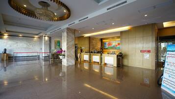 A hotel lobby with a reception desk, a chandelier, marble columns, and a red rope barrier.
