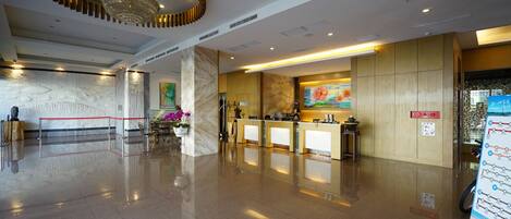 A hotel lobby with a reception desk, a chandelier, marble columns, and a red rope barrier.