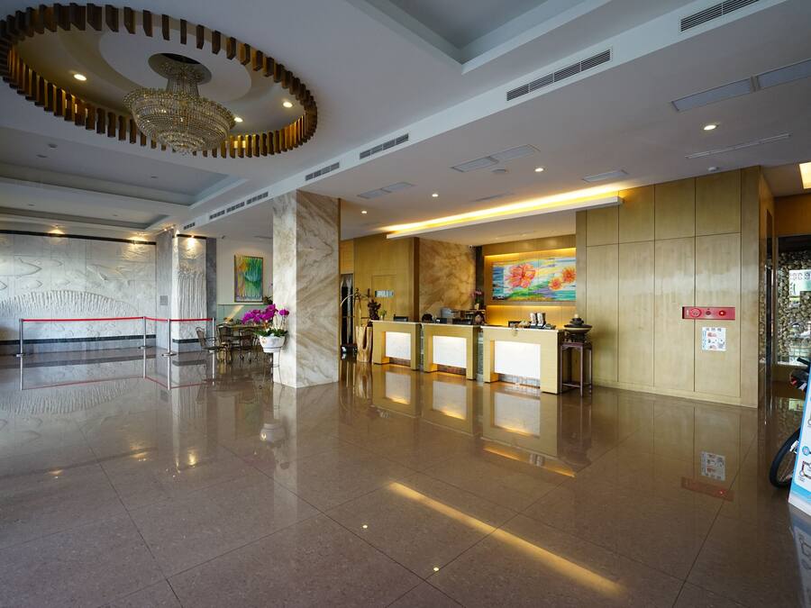A hotel lobby with a reception desk, a chandelier, marble columns, and a red rope barrier.