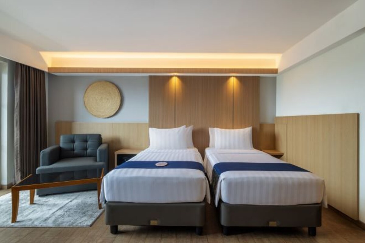 Ett hotellrum med två sängar, en soffa, en rund väggdekoration och en sänggavel i trä.
