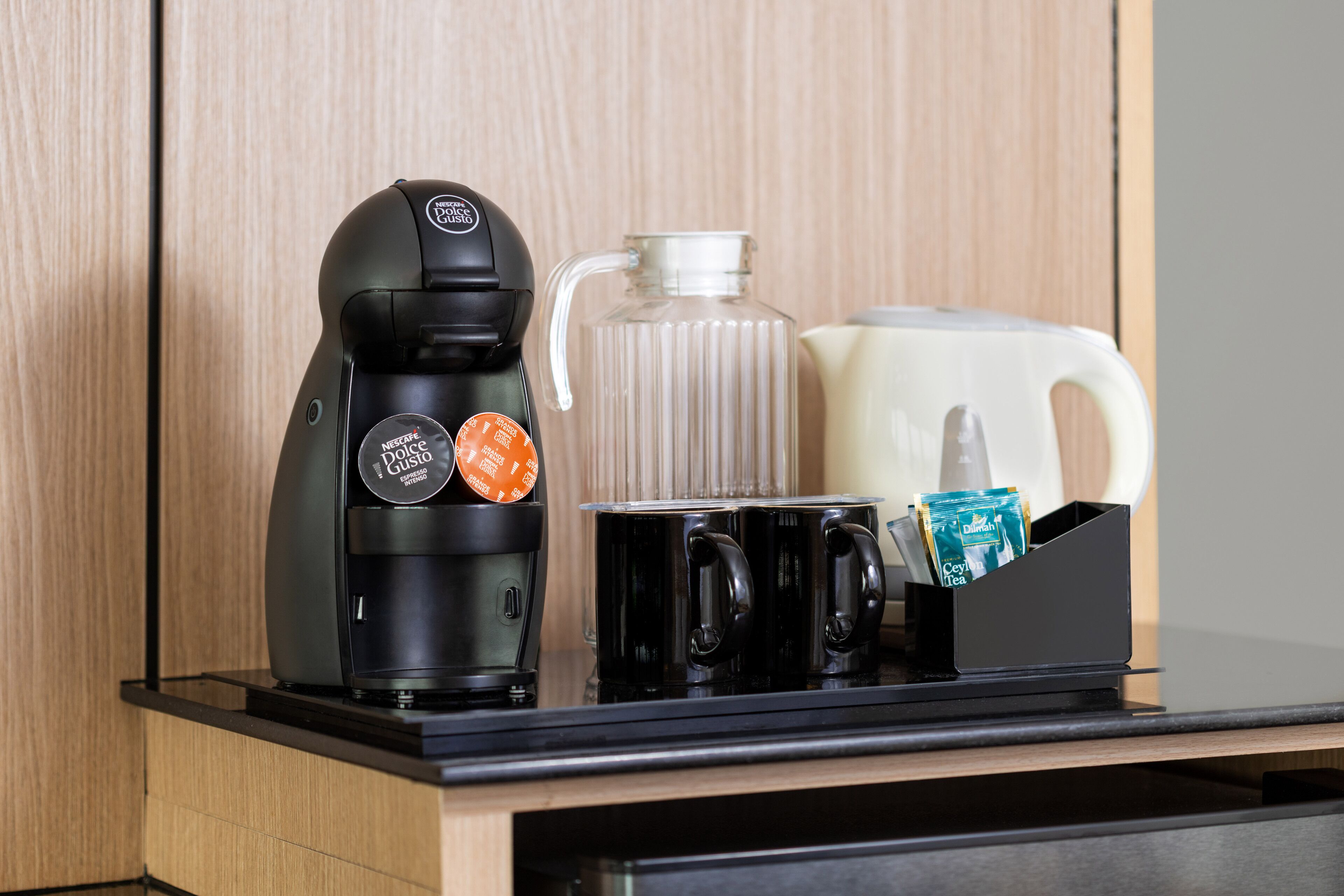 A coffee maker, a glass carafe, and a mug holder with coffee pods on a kitchen counter.